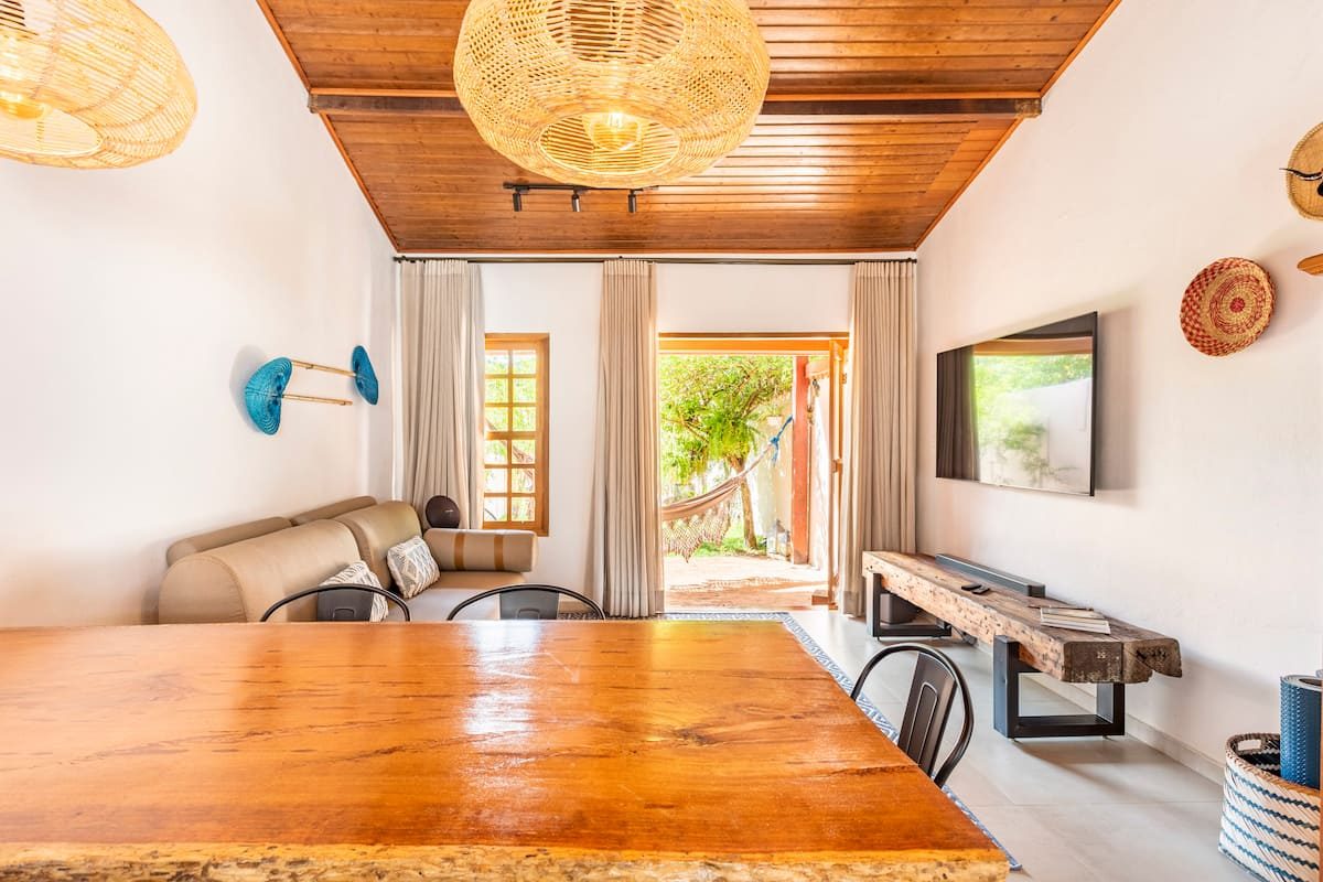 Sala de jantar da Casa Boutique com mesa de madeira maciça, luminárias de palha e porta aberta para o jardim