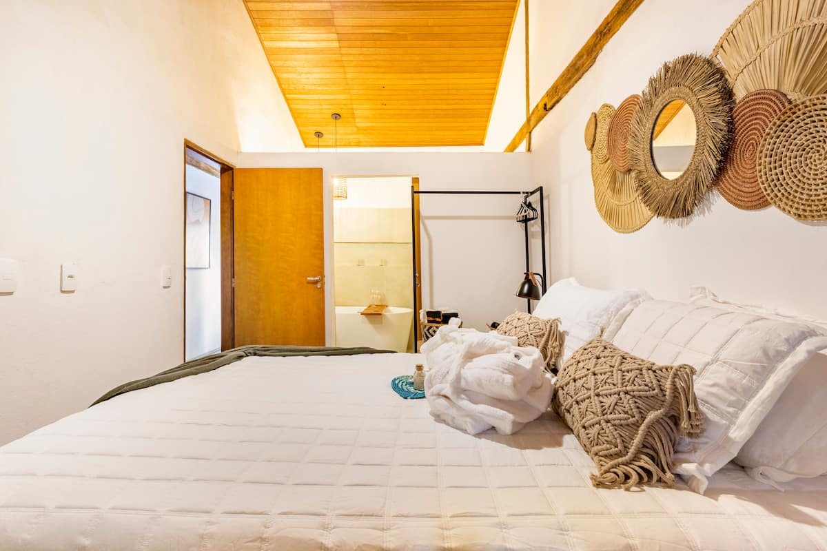 Quarto da Casa Boutique com cama branca e porta aberta para o banheiro com banheira