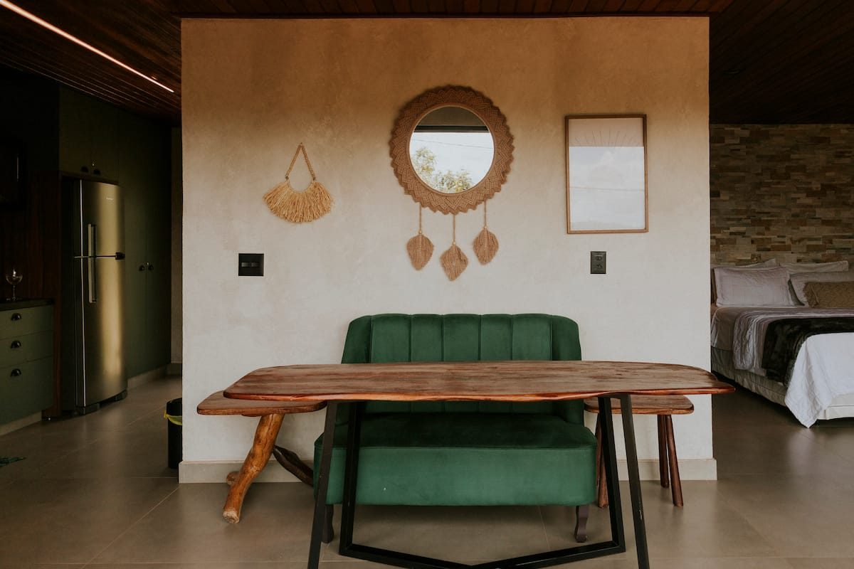 Cantinho de estar da Casa Jade com espelho de macramê, sofá verde e mesa de madeira de borda viva