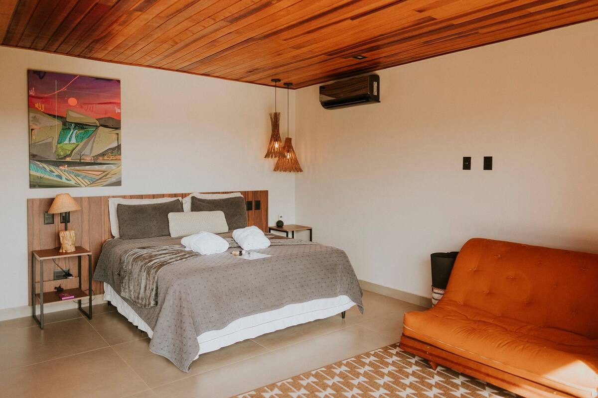 Quarto amplo da Casa Turmalina com sofá futon laranja e teto de madeira